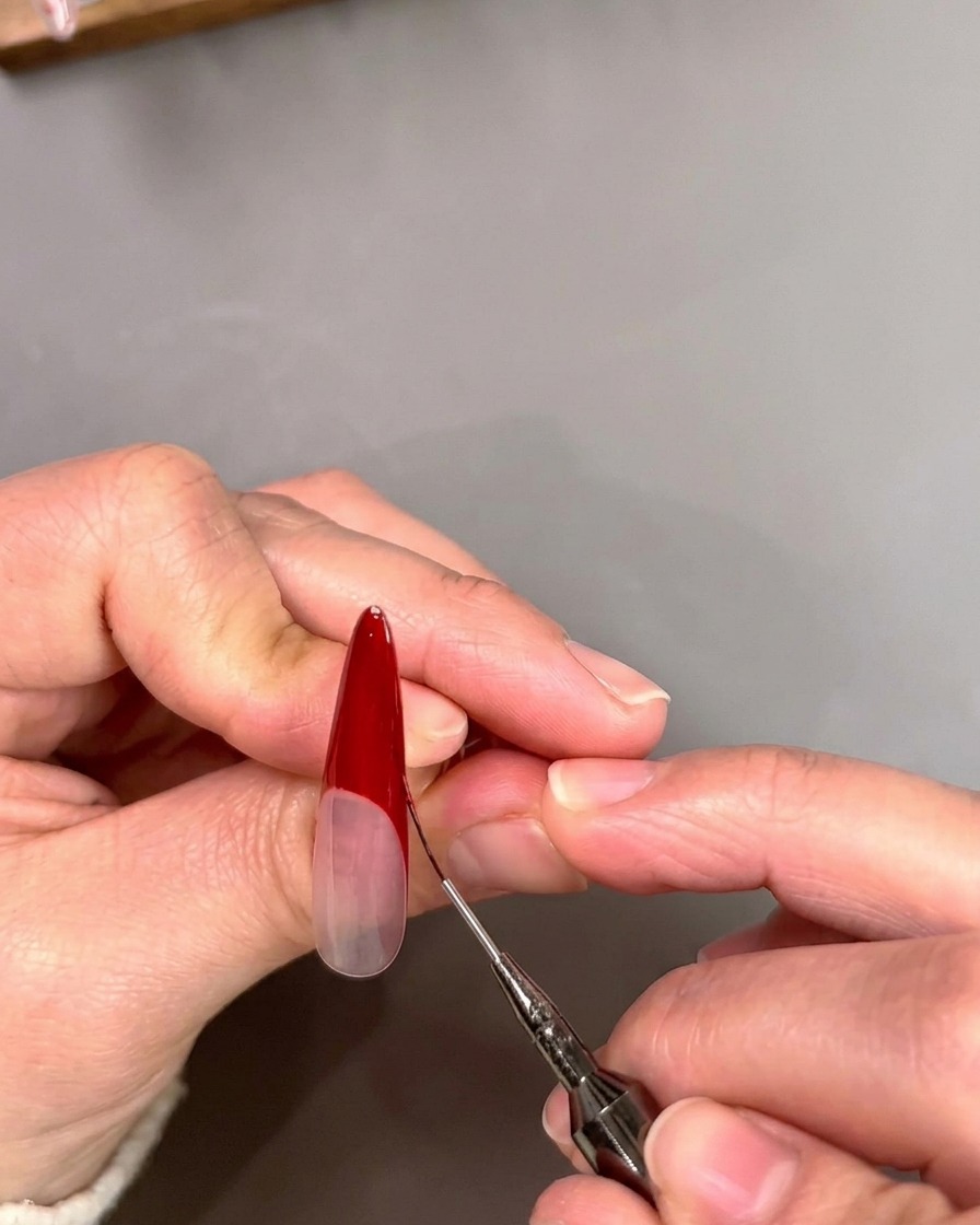 Un pincel liner fino afinando el borde interno de una punta francesa roja en forma de V.