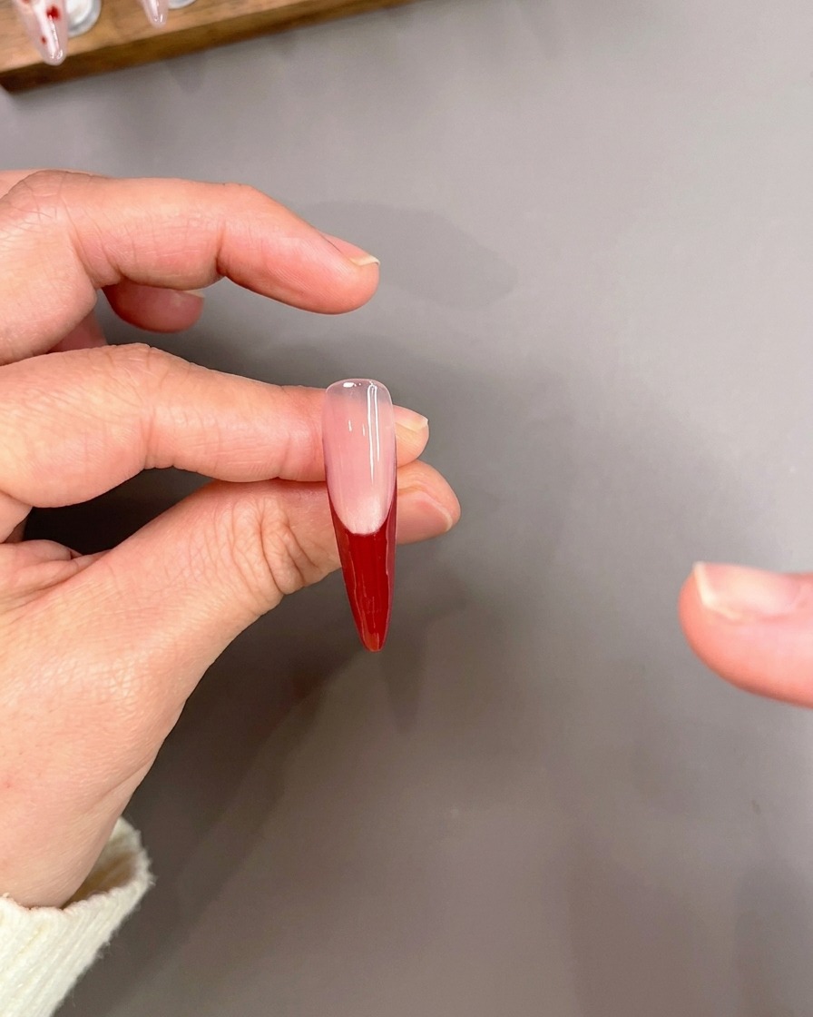 Un pincel liner dibujando cuidadosamente líneas rojas finas sobre una uña con base de manicura francesa.