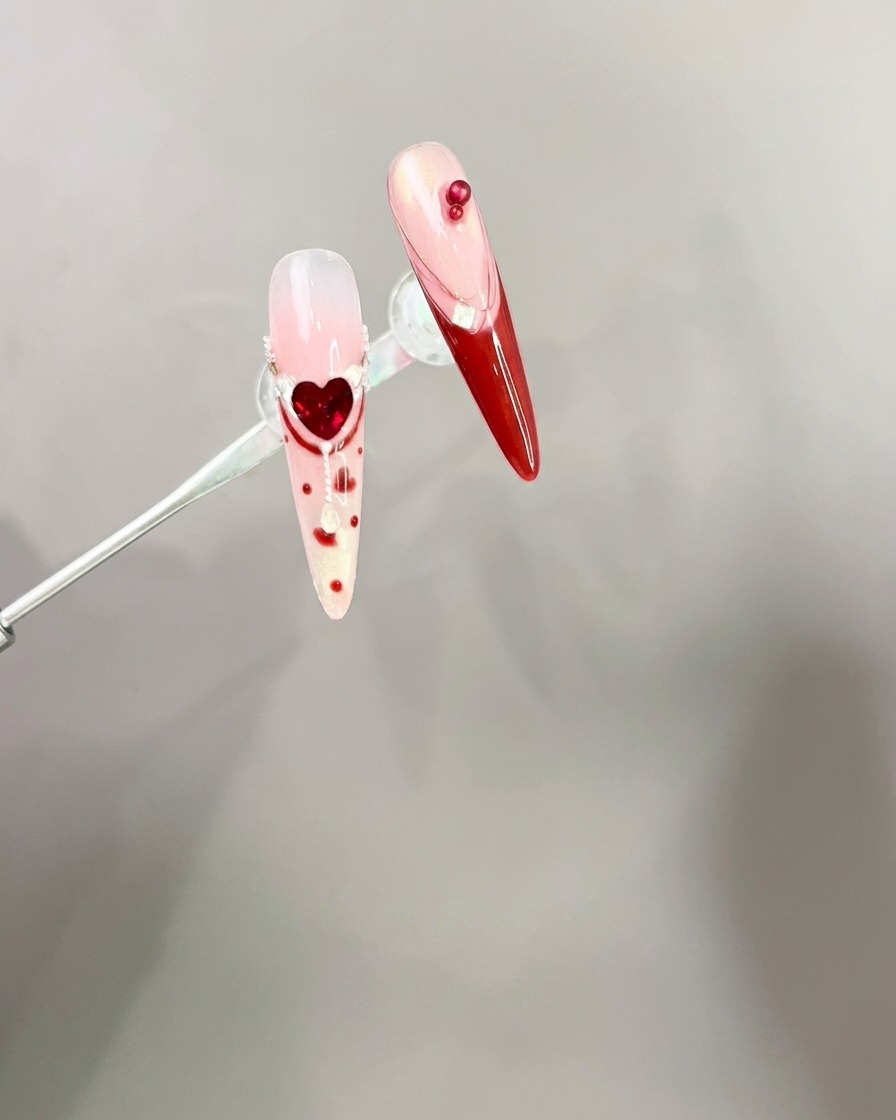 Pinzas colocando un dije de lazo rojo 3D sobre una uña manicurada.