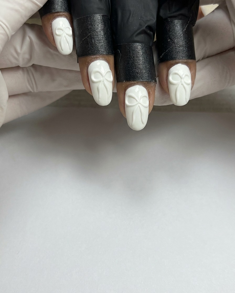 Un pincel de uñas aplicando una capa suave de esmalte en gel blanco sobre una uña natural preparada.