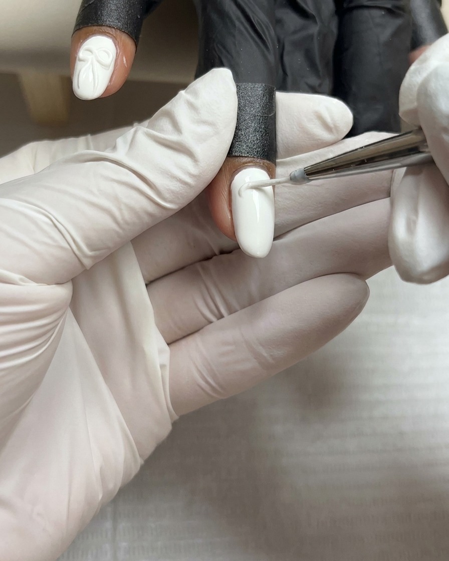 Una gota pequeña y precisa de gel de esculpido blanco espeso descansando en el centro de una uña pintada de blanco.