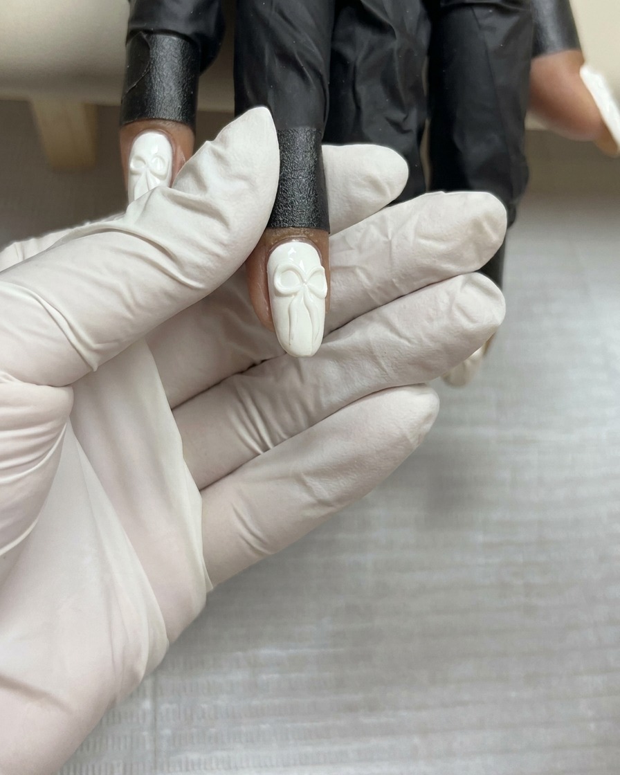 Vista cenital de un diseño de lazo de gel 3D completado sobre una uña blanca, sostenida firmemente antes del curado final.