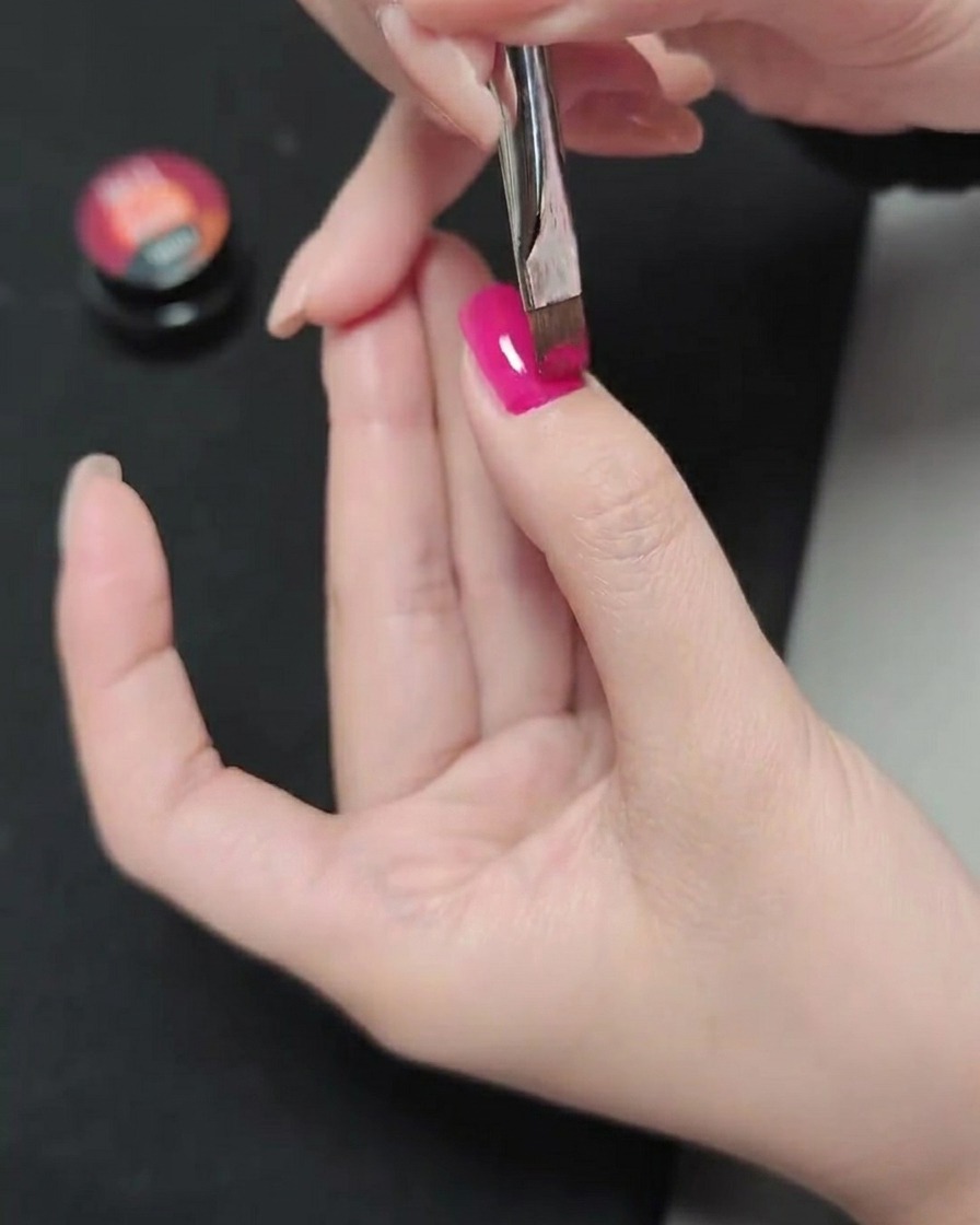 Un pincel aplicando una segunda capa de esmalte de gel magenta sobre la capa previamente curada.