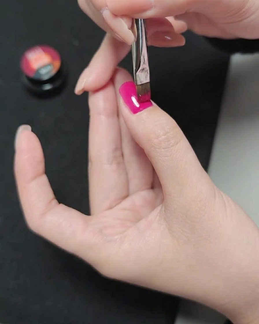 Un pincel aplicando una tercera capa de esmalte de gel magenta, creando un acabado de color suave y saturado.