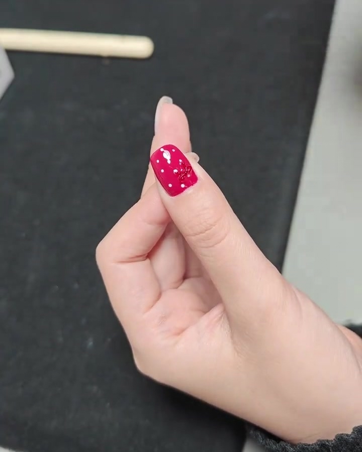 Un primer plano de una mano con una uña terminada de lunares con lazo dentro de una lámpara de uñas profesional UV.
