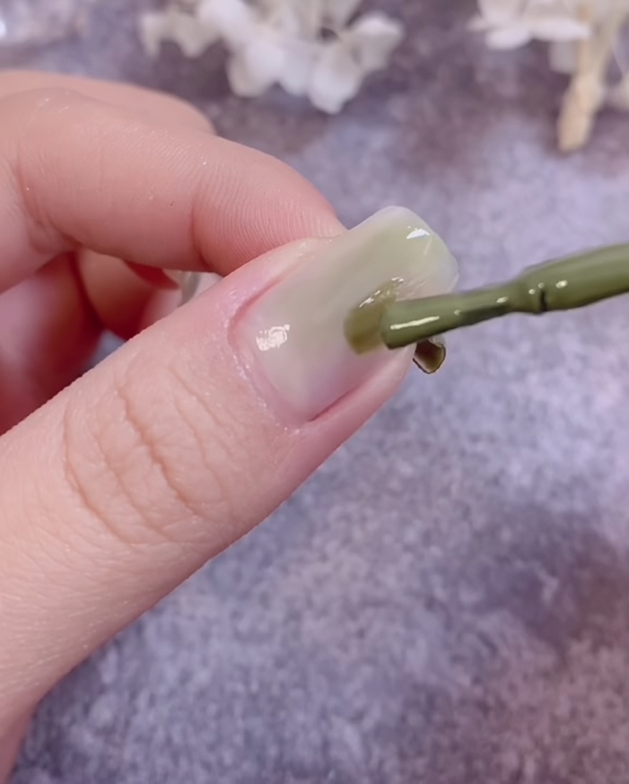 Un pincel difuminando esmalte de gel verde sobre una superficie de uña para crear un efecto degradado.