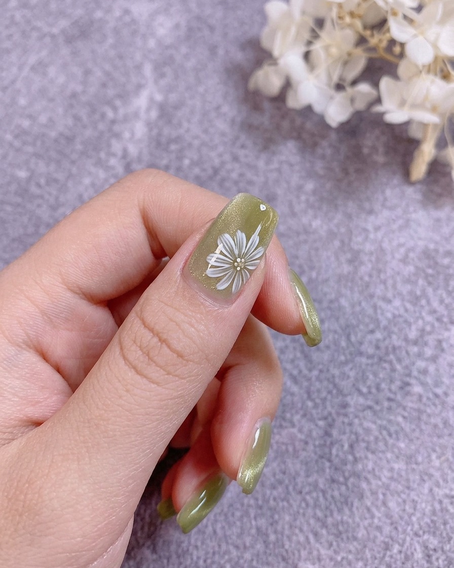 Un pincel de uñas aplicando un top coat transparente y duro sobre un diseño floral pintado.