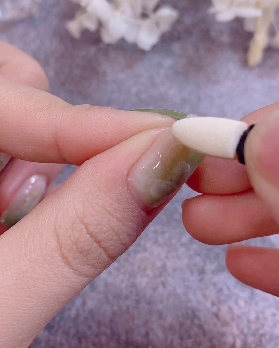 Un aplicador de silicona tipo sombra de ojos siendo usado para pulir polvo cromado metálico sobre una uña pintada con gel.