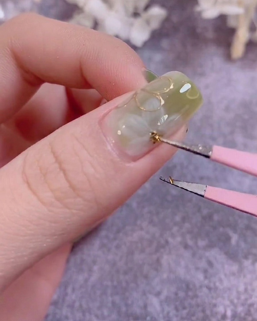 Un pincel de detalle pintando pequeñas hojas verdes sobre una superficie de uña manicurada.