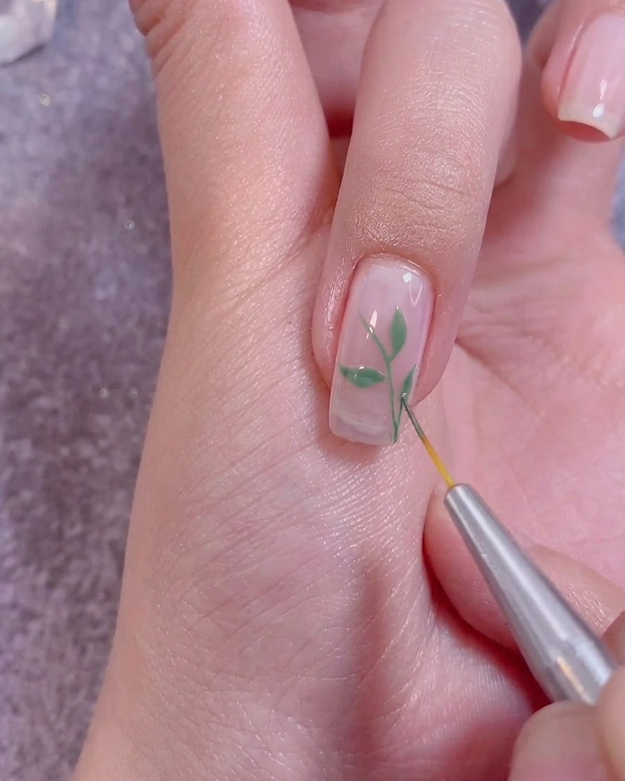 Aplicando un top coat transparente sobre el arte de uñas terminado con un pincel profesional.