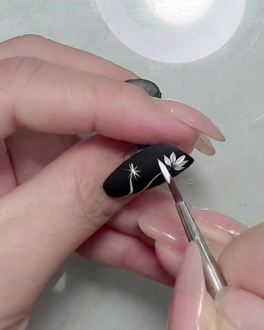 Primer plano de una flor de margarita blanca totalmente formada sobre una uña negra mate.