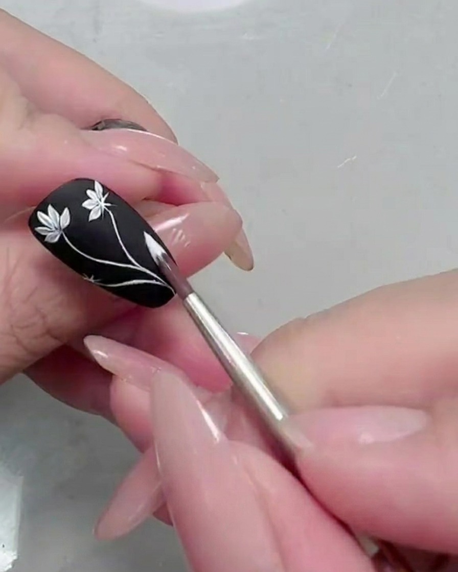 Primer plano de una segunda flor de margarita siendo pintada sobre la uña negra.