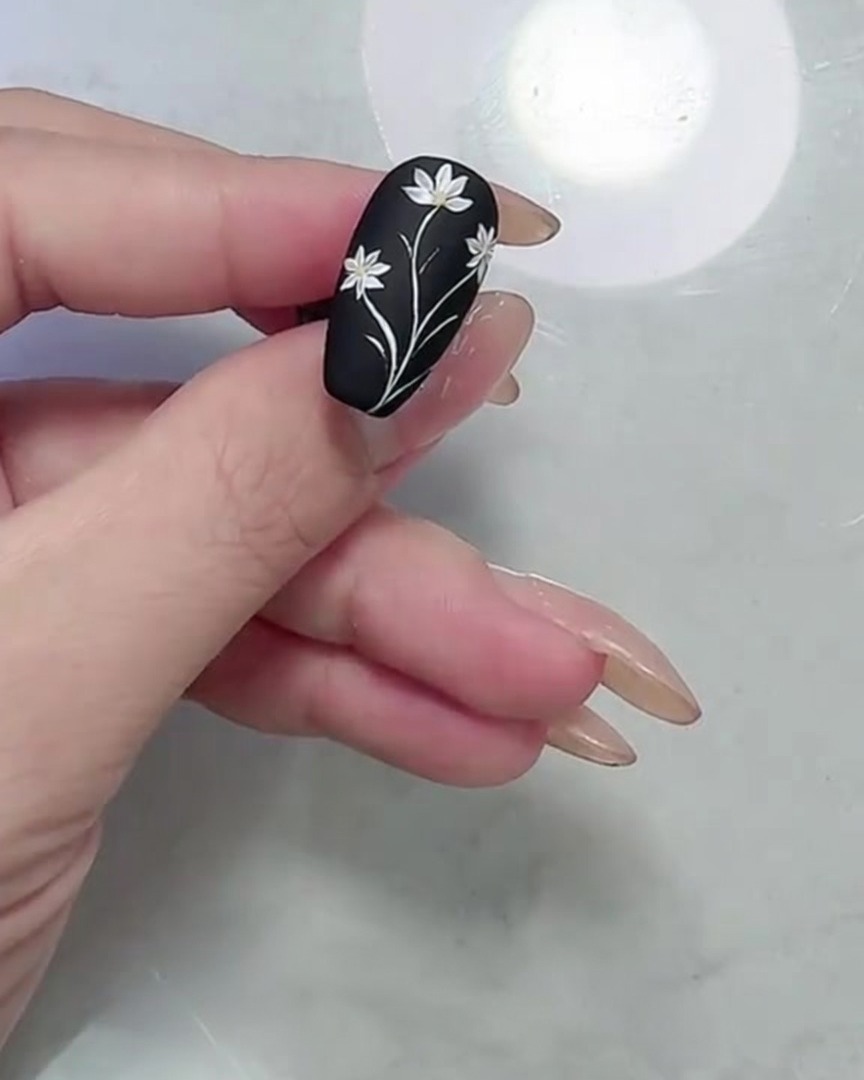 Una toma macro que muestra el diseño final de margarita y hojas en una uña negra mate, enfocándose en los bordes definidos de pétalos y hojas.