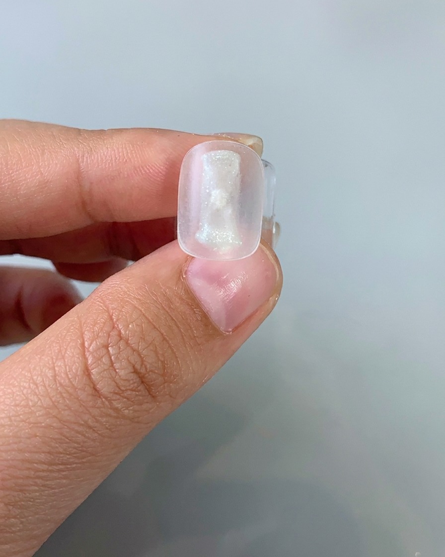 Un pincel aplicando una capa fina de gel cat-eye de tono claro sobre una uña.