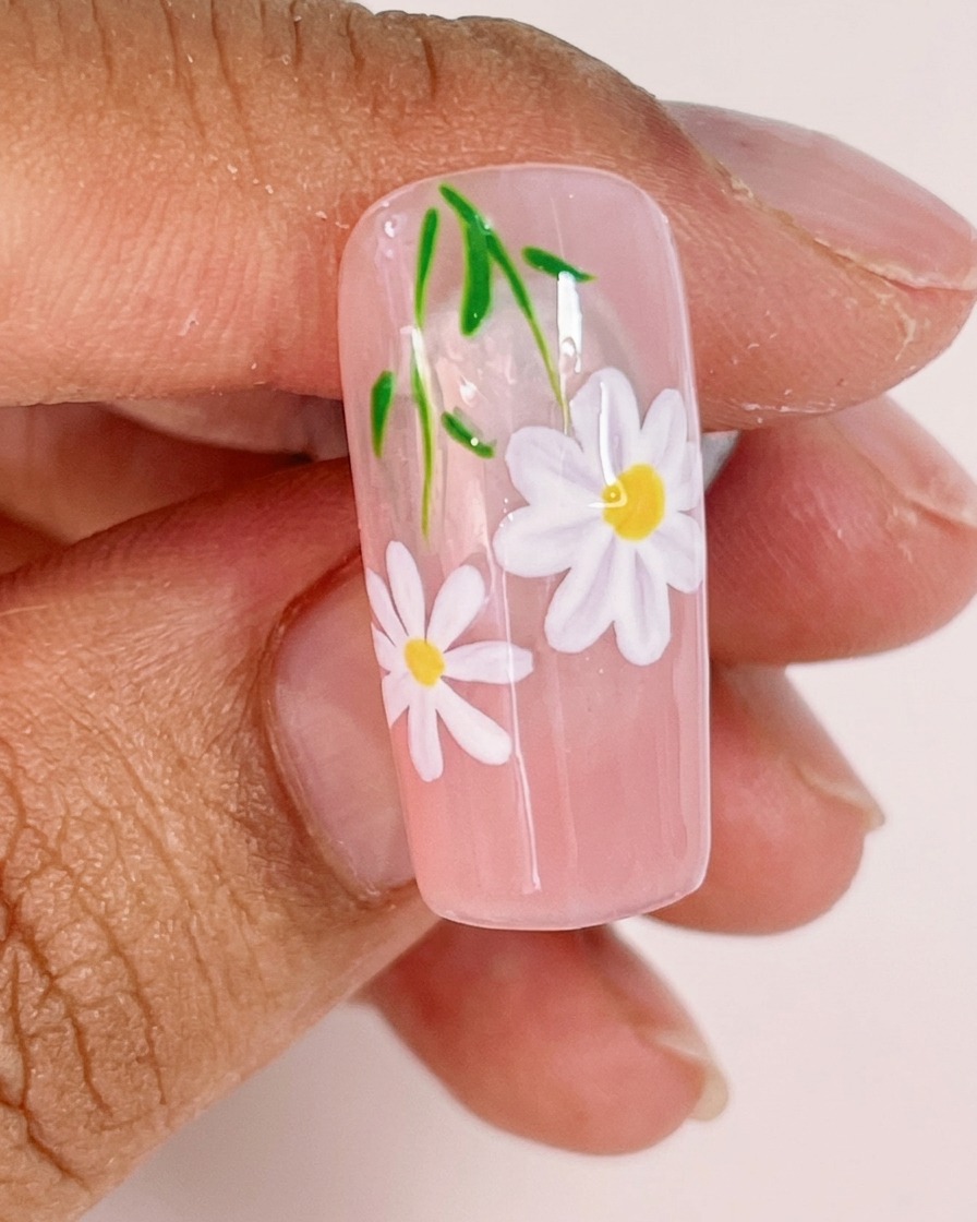 Primer plano mostrando un pincel liner fino añadiendo tallos verdes delgados y pequeñas hojas al diseño de uñas con margaritas.