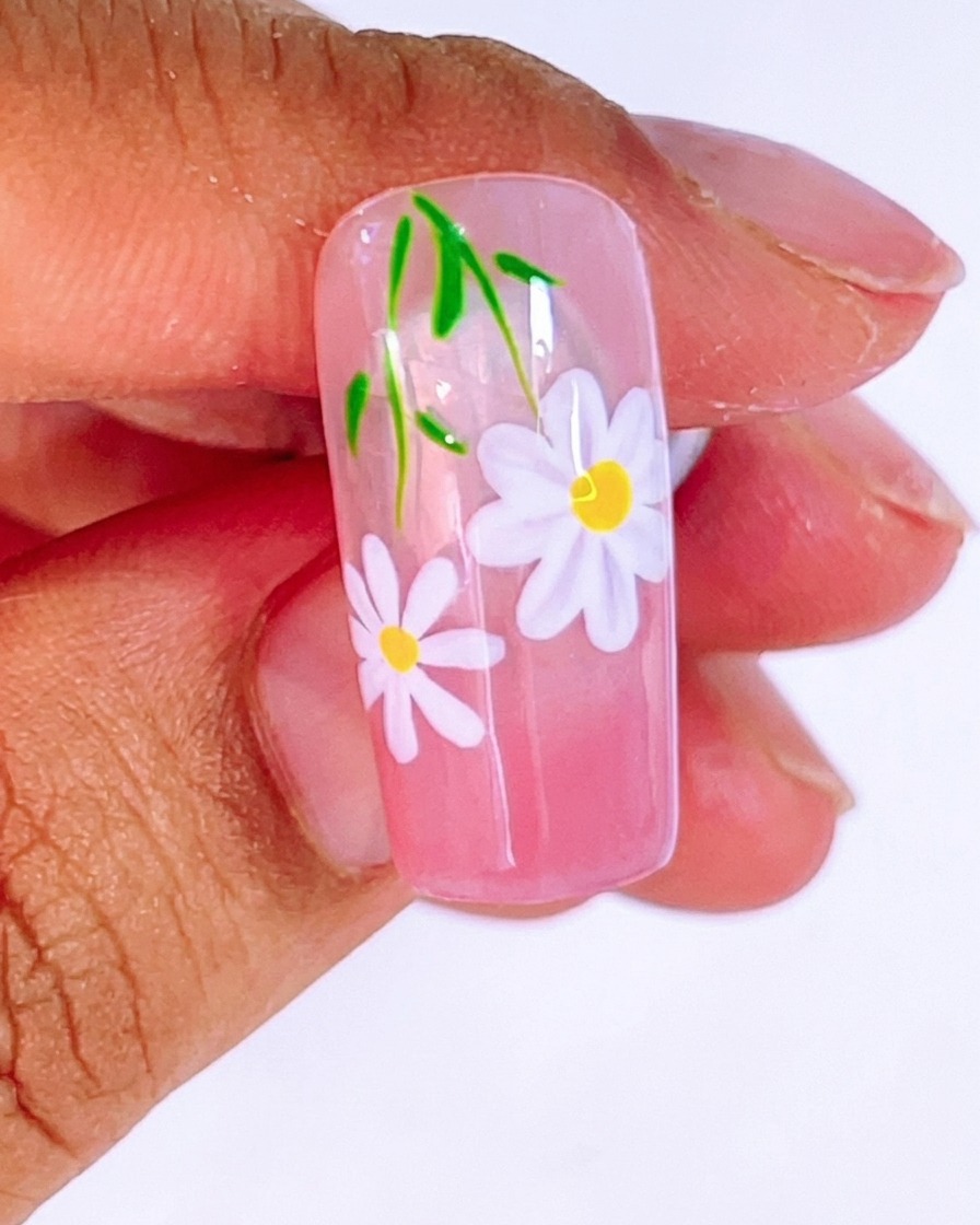 Un pincel aplicando una capa gruesa y brillante de top coat transparente sobre el diseño terminado de margaritas y hojas.