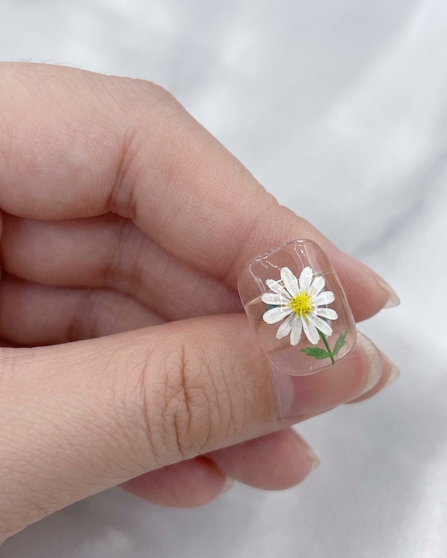 Un pincel aplicando una capa superior transparente y brillante sobre un diseño de uñas de margarita terminado.