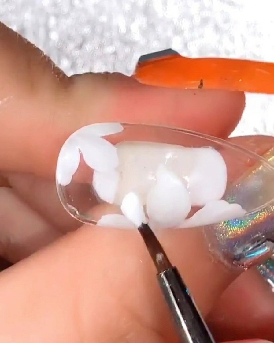Pincel de detalle añadiendo más pétalos de gel blanco sobre el diseño curado para dar volumen.