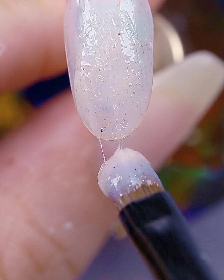 Un pincel de uñas aplicando una segunda capa de gel texturizado, con la superficie de la uña lista para el curado.