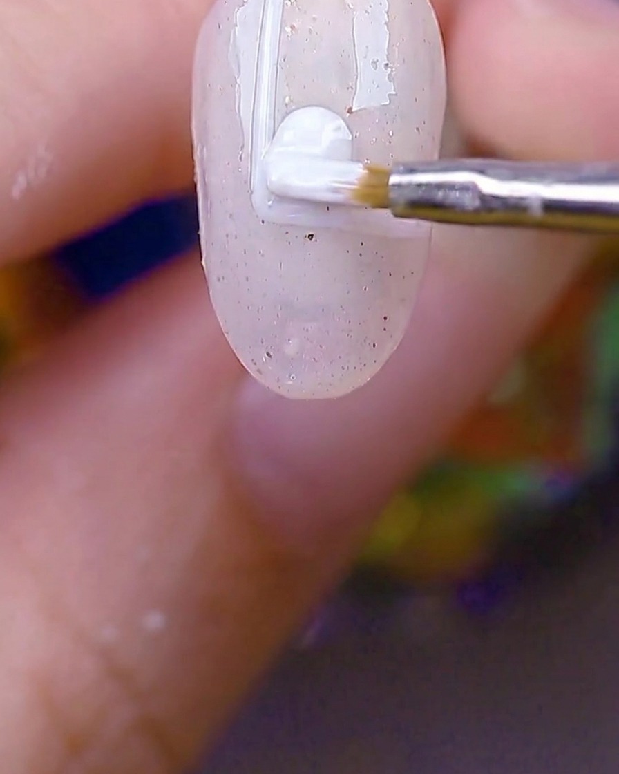 Un pincel redondo pequeño rellenando el rectángulo de borde blanco en la uña con gel blanco opaco.