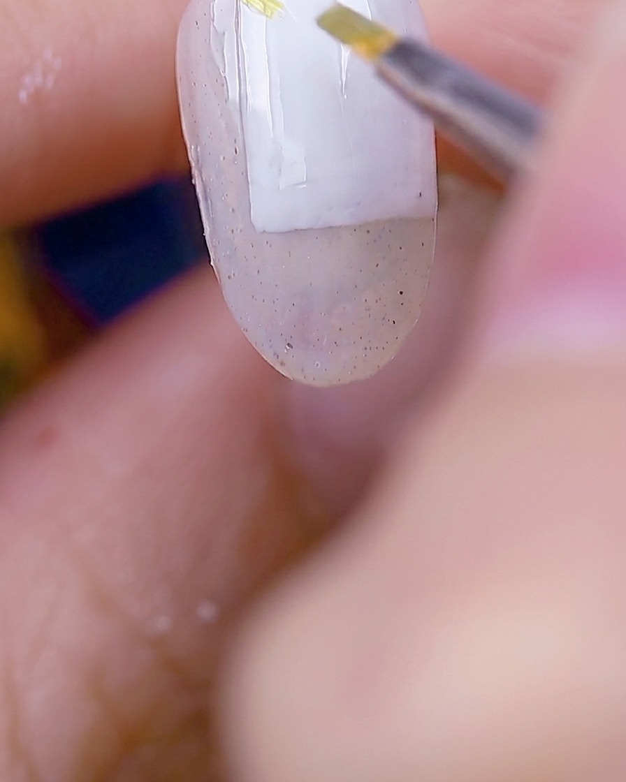 Un pincel aplicando gel color verde musgo para crear delicadas formas de hojas sobre la superficie de la uña.