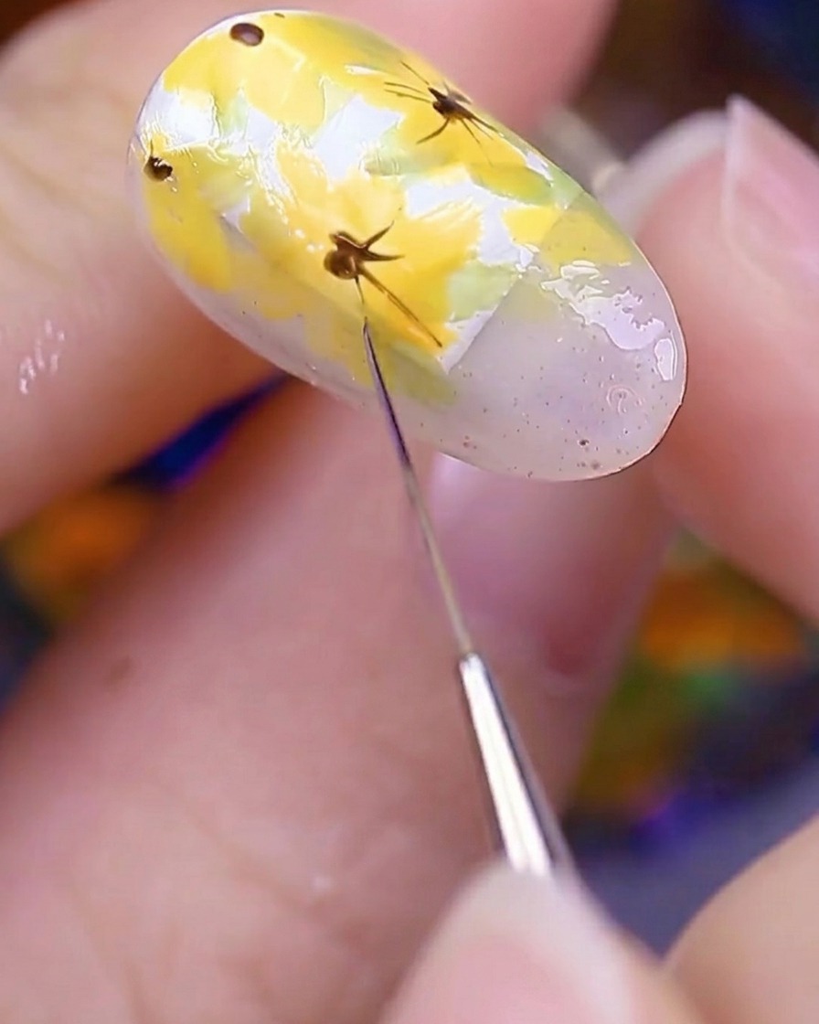 Primer plano de la uña pintada bajo una lámpara UV para curar los detalles florales recién aplicados.