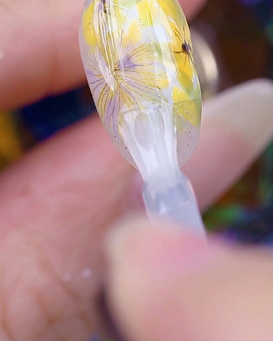 Un pincel aplicando una capa superior transparente y brillante sobre el diseño de uñas de margaritas terminado.