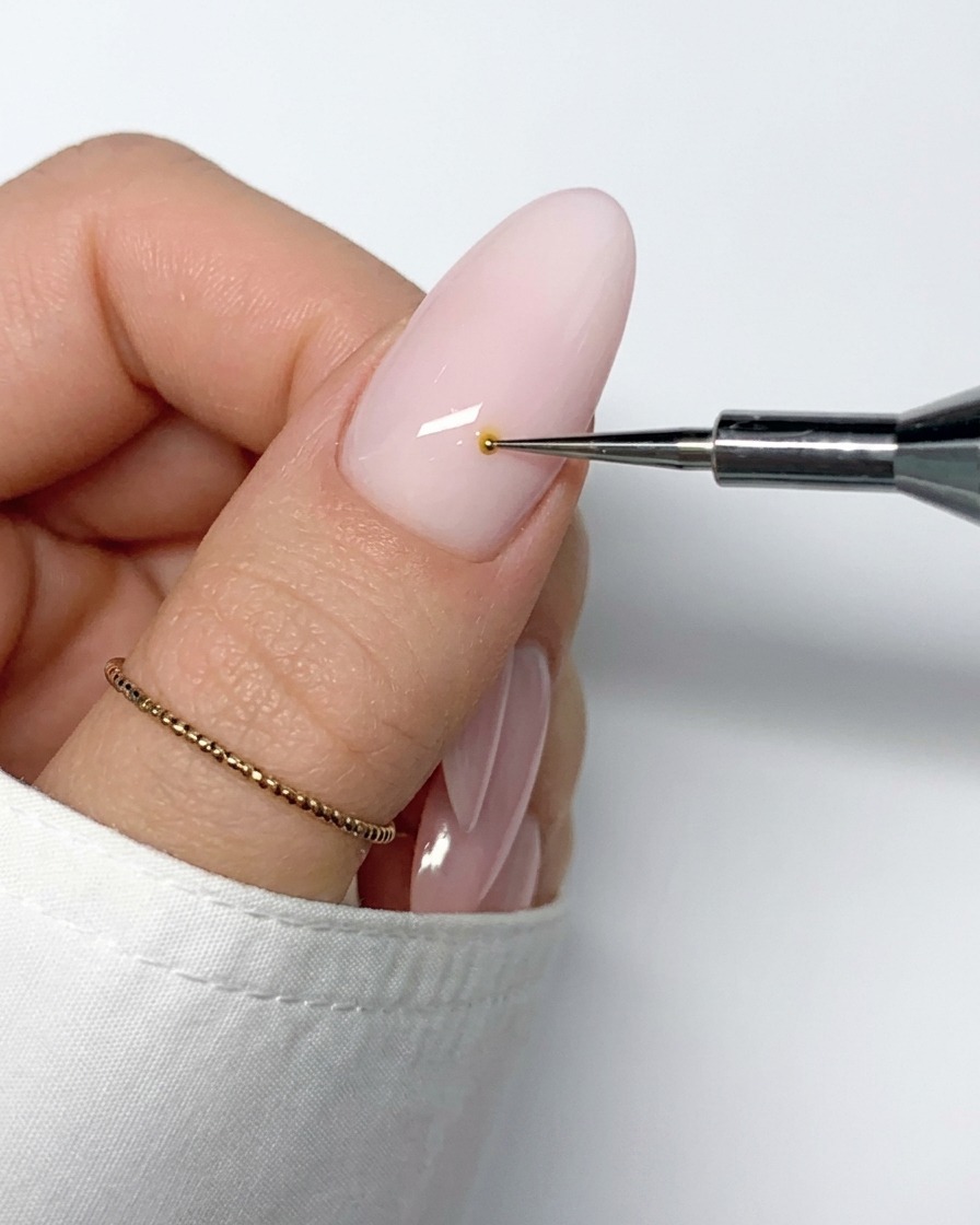 Un pincel fino de nail art trazando una línea de esmalte de gel blanco hacia afuera desde el centro amarillo.