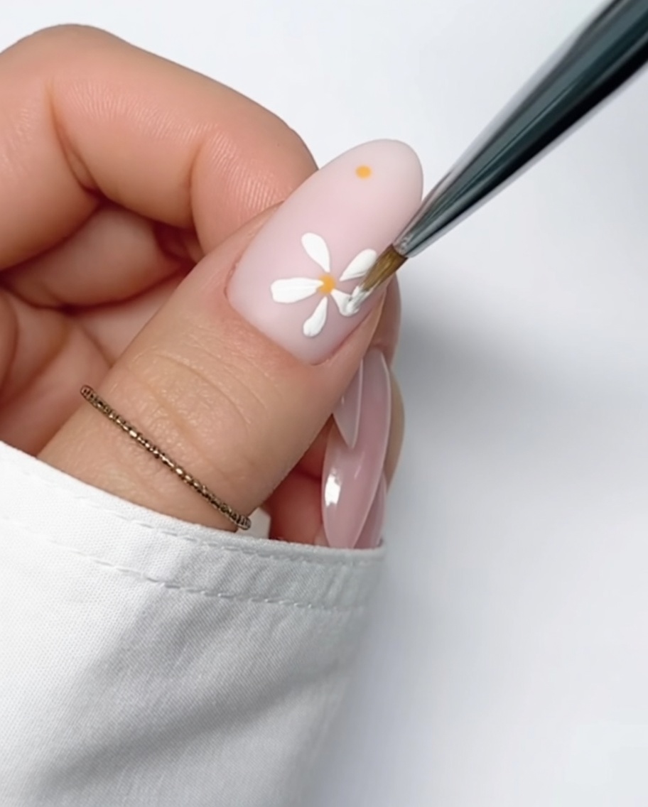 Primer plano de una uña color nude con un pequeño punto amarillo de gel, listo para pintar los pétalos.