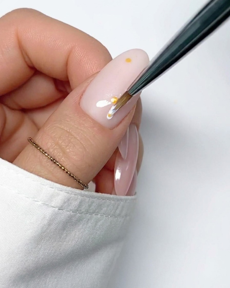 Un pincel de detalle aplicando un trazo fino de gel blanco desde el centro amarillo para formar el primer pétalo.