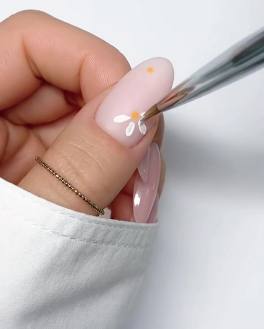 Una margarita blanca completa con centro amarillo pintada sobre una base nude.