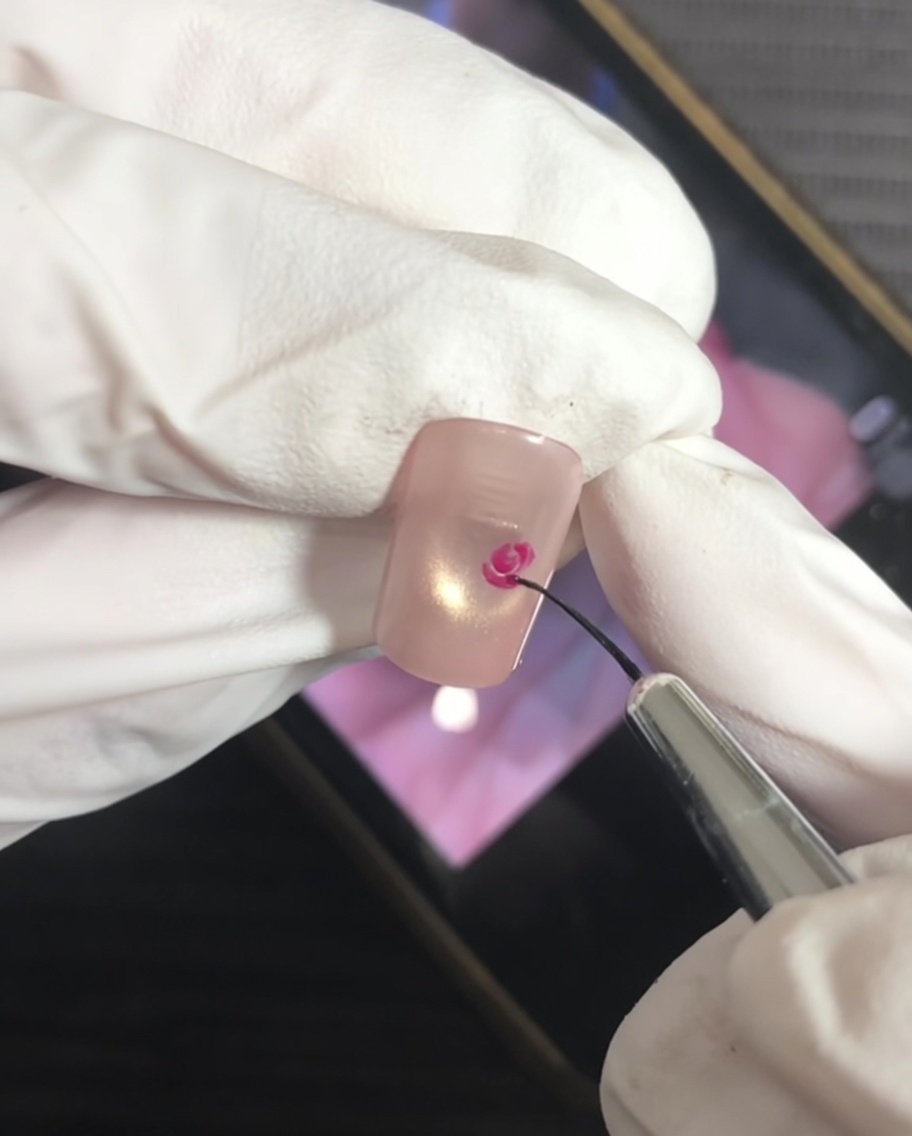 Pincel fino añadiendo trazos en forma de corchete al centro magenta para formar pétalos.