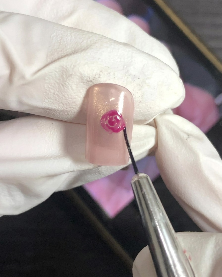 Pincel de nail art difuminando los bordes de un pétalo magenta sobre base nude.