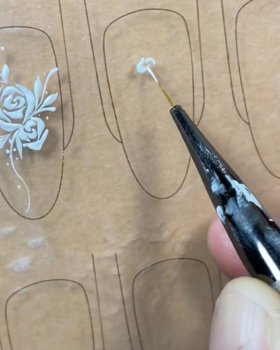 Primer plano de un pincel liner aplicando un pequeño punto de gel blanco en el centro de un tip de uña transparente.
