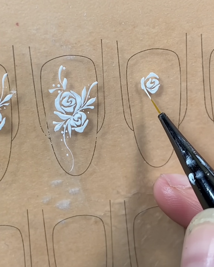 Un pincel liner añadiendo una línea curva debajo del capullo central para cerrar la forma de la rosa.