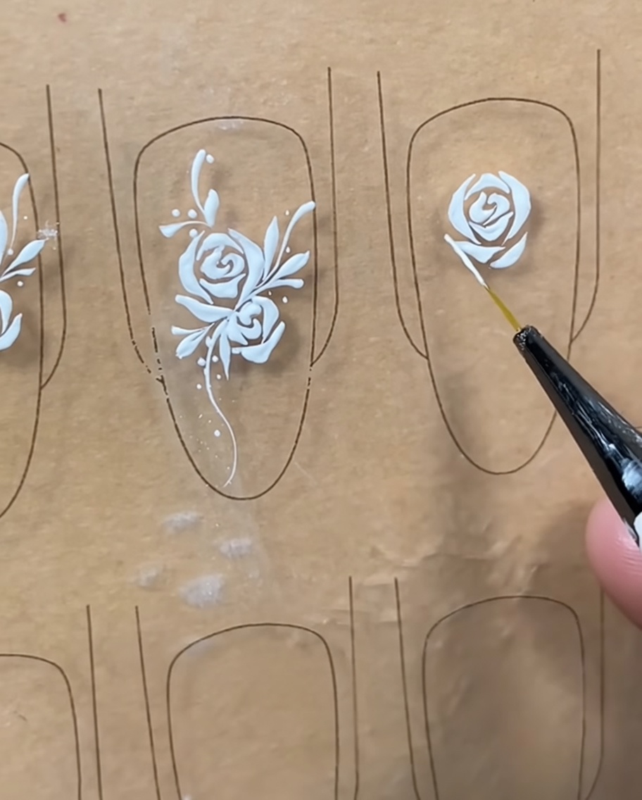 Primer plano de un pincel liner añadiendo detalles finos en blanco a los bordes exteriores de un diseño de rosa en un tip.