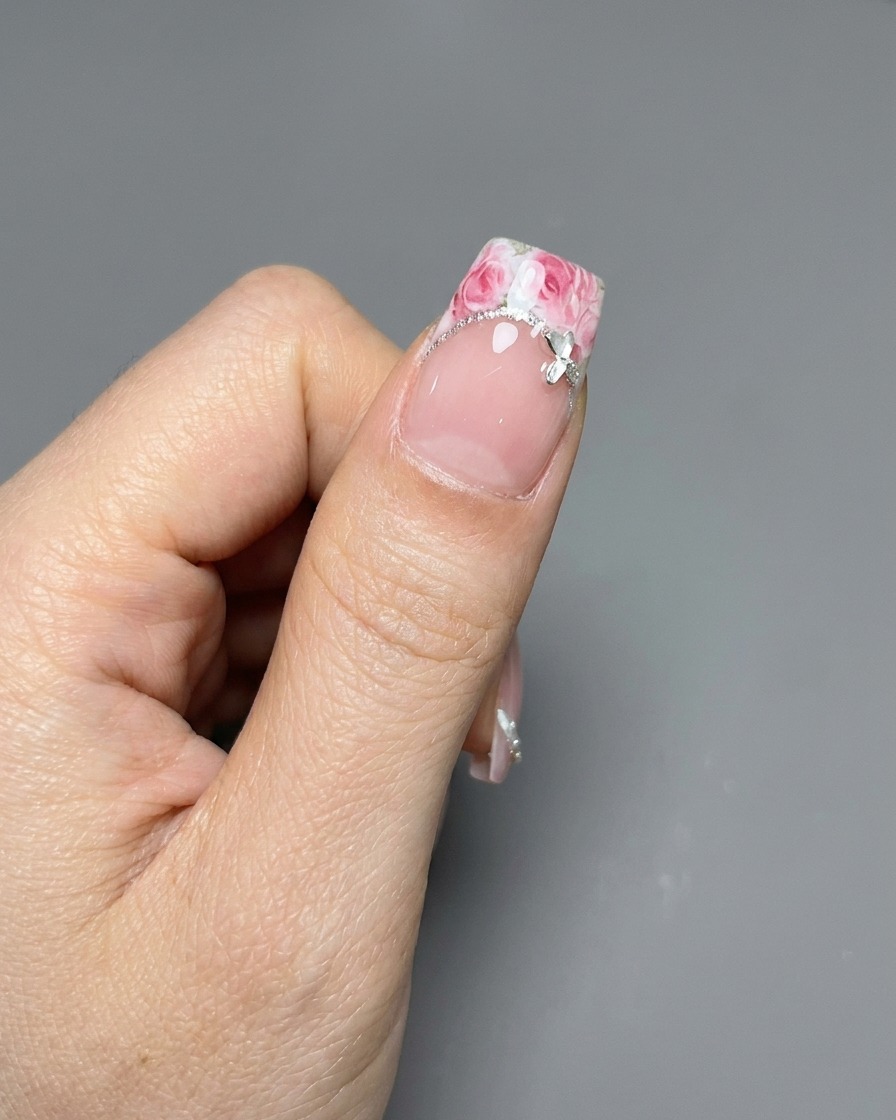 Un par de pinzas colocando una pegatina con patrón de rosa sobre una punta francesa manicurada.