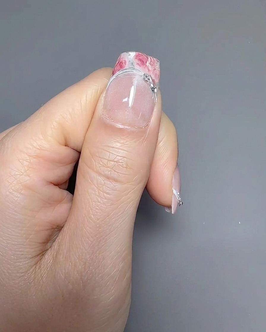 Un pincel liner fino trazando cuidadosamente la línea de la sonrisa en una uña con manicura francesa.