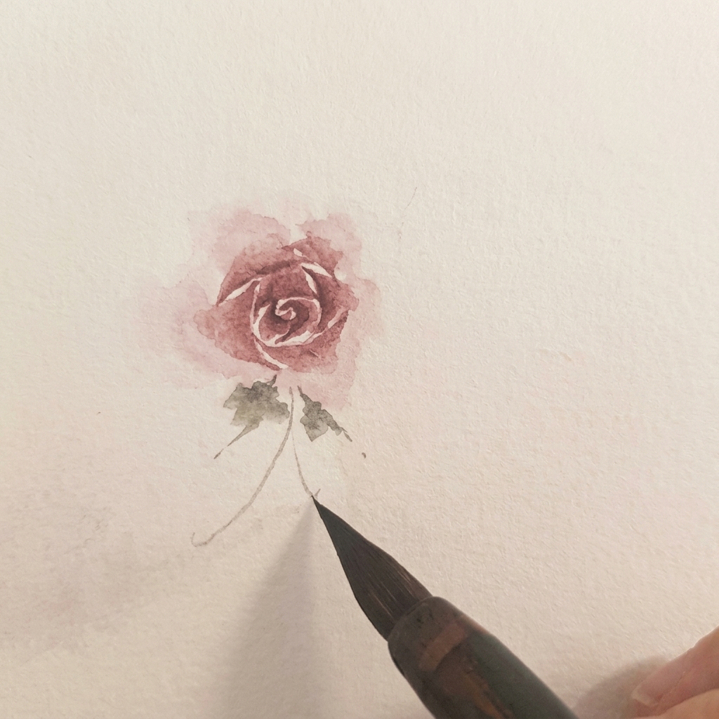 Dos pequeñas hojas verdes de acuarela pintadas en la base de una rosa terminada.