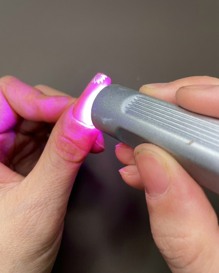 Una herramienta de nail art aplicando un pequeño punto de gel de construcción transparente en la superficie de la uña cerca de las flores pintadas.