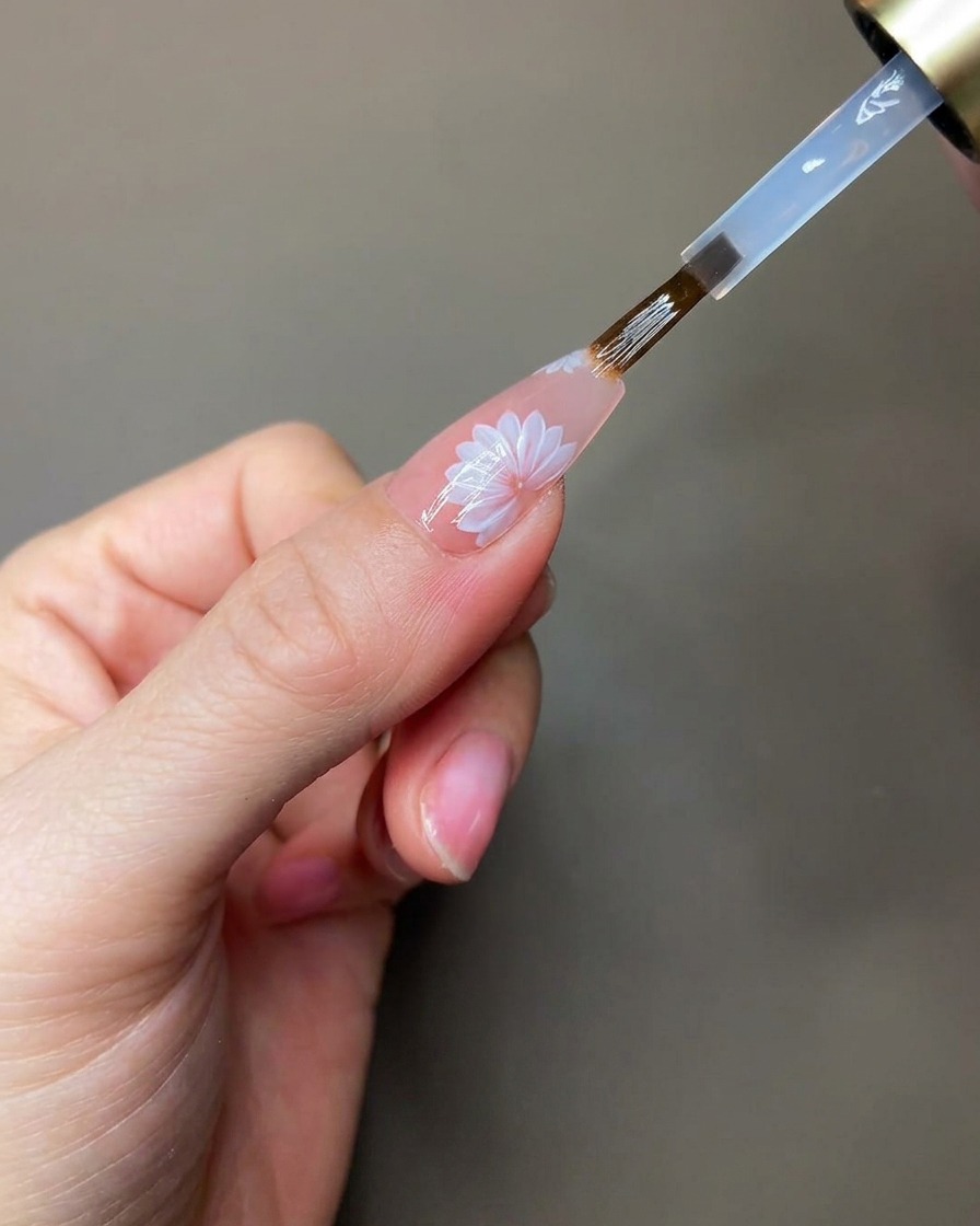Una mano posicionada bajo una lámpara UV/LED portátil mientras se curan los detalles de gel de construcción transparente.