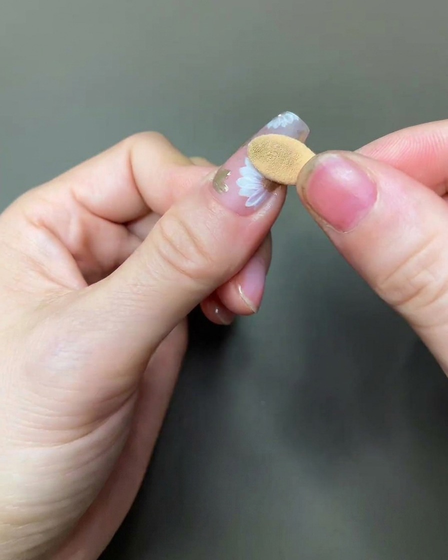 Un primer plano de un aplicador de espuma puliendo cuidadosamente pigmento cromo dorado sobre el centro de un diseño de margarita pintado.