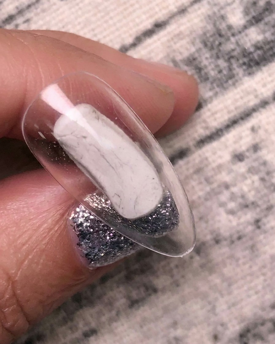 Un pincel aplicando gel adhesivo de transferencia transparente sobre un tip de uña claro.