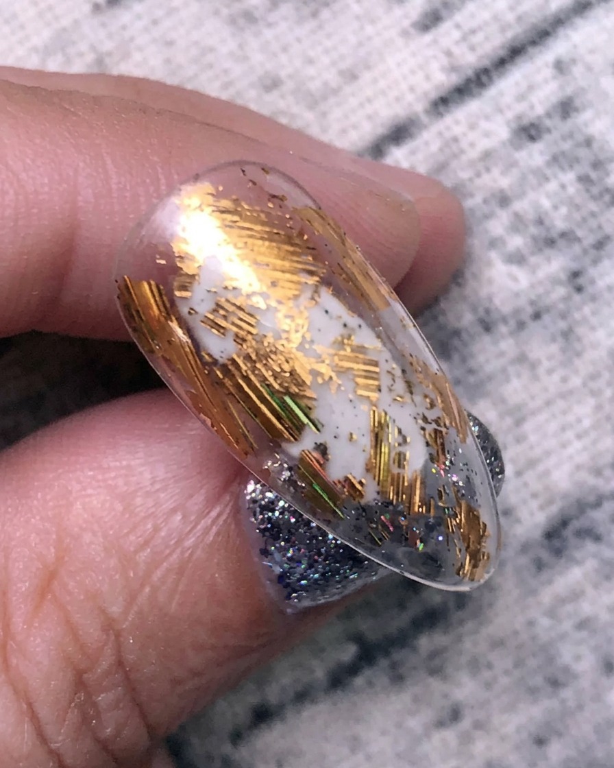 Aplicando lámina de transferencia dorada sobre la superficie de una uña usando una herramienta de silicona.