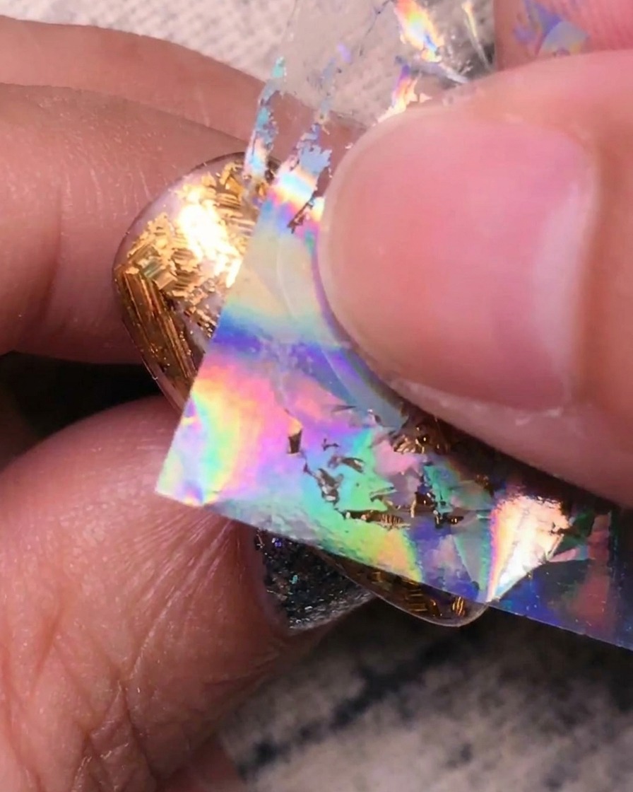 Presionando lámina plateada holográfica sobre las secciones transparentes restantes de la uña.