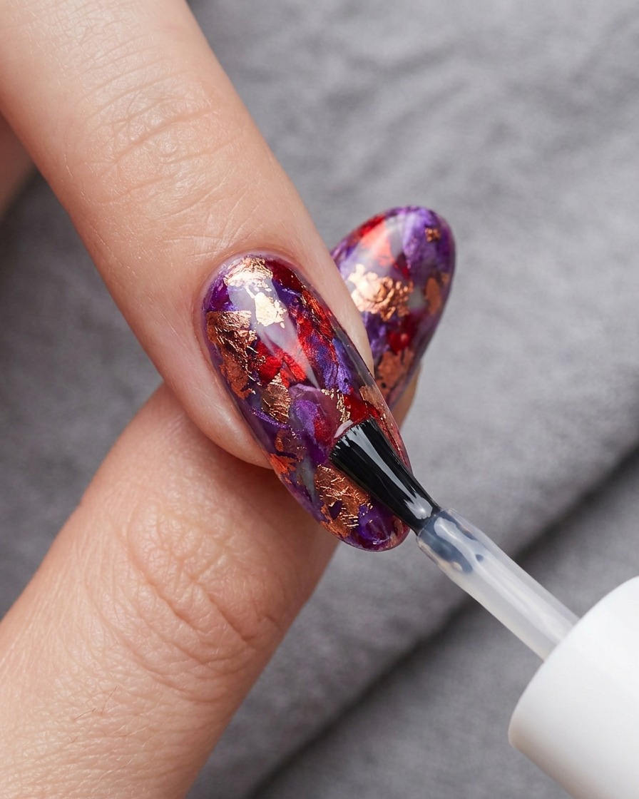 Un pincel aplicando un top coat transparente y brillante sobre el arte de blooming gel rojo y azul terminado.