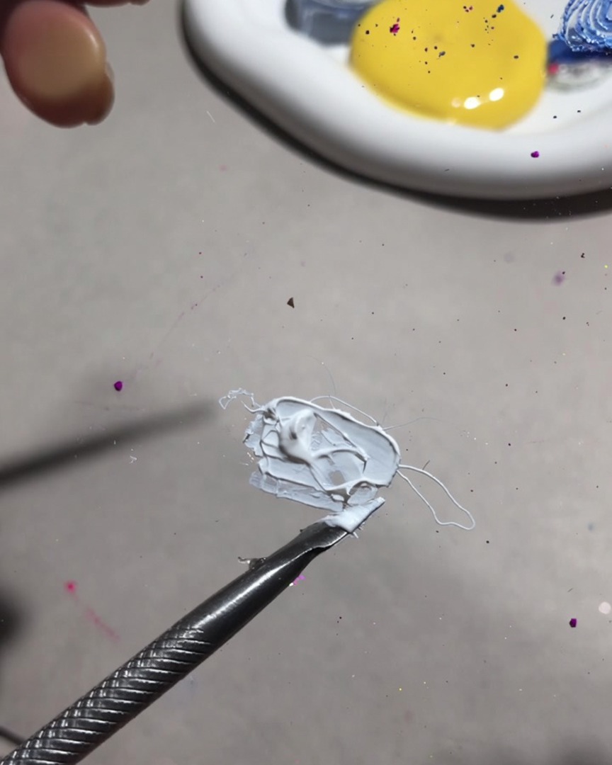 Primer plano de una herramienta de mezcla combinando gel blanco de pintura y gel de frutas en una textura suave y cremosa.