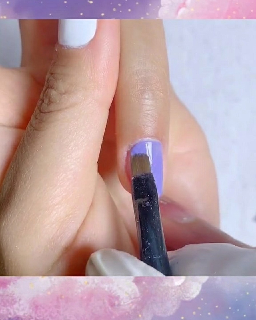 Primer plano detallado de un pincel delineador aplicando una segunda capa suave de esmalte gel azul-morado vibrante.