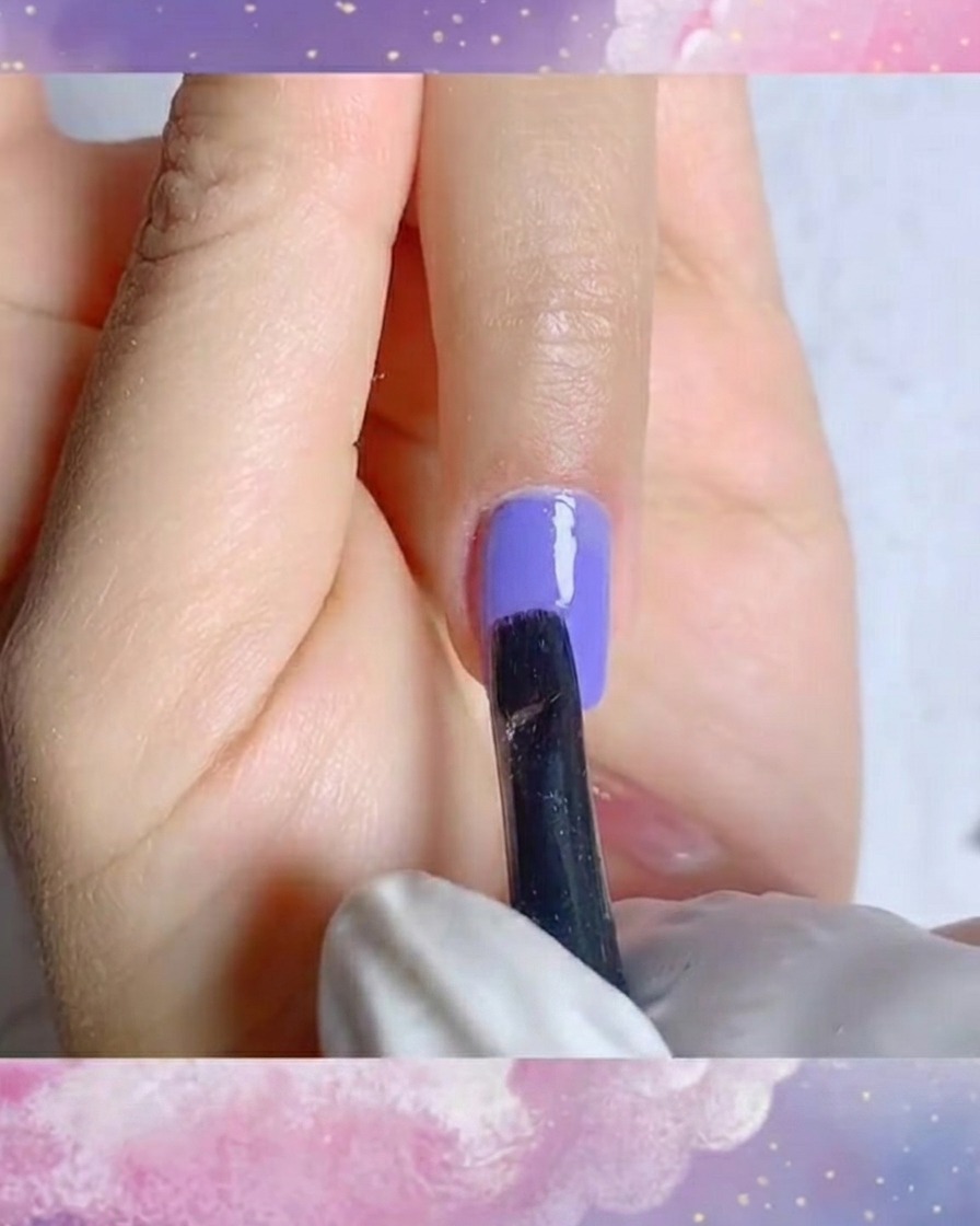 Una toma de primer plano de un pincel delineador fino creando trazos de pétalos blancos precisos sobre una base gel morada.