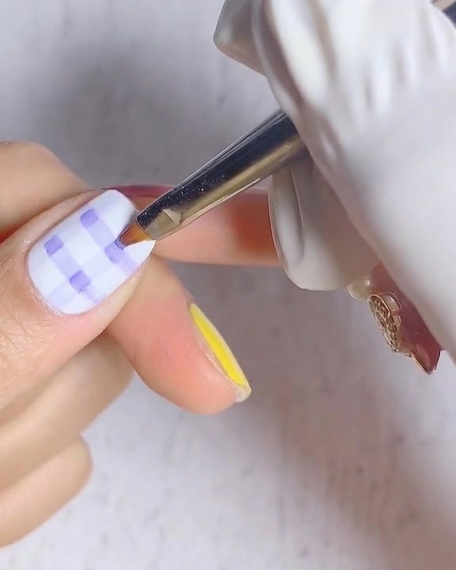 Una vista de primer plano de una uña con un patrón de cuadros azul y blanco colocada bajo una lámpara de uñas UV.